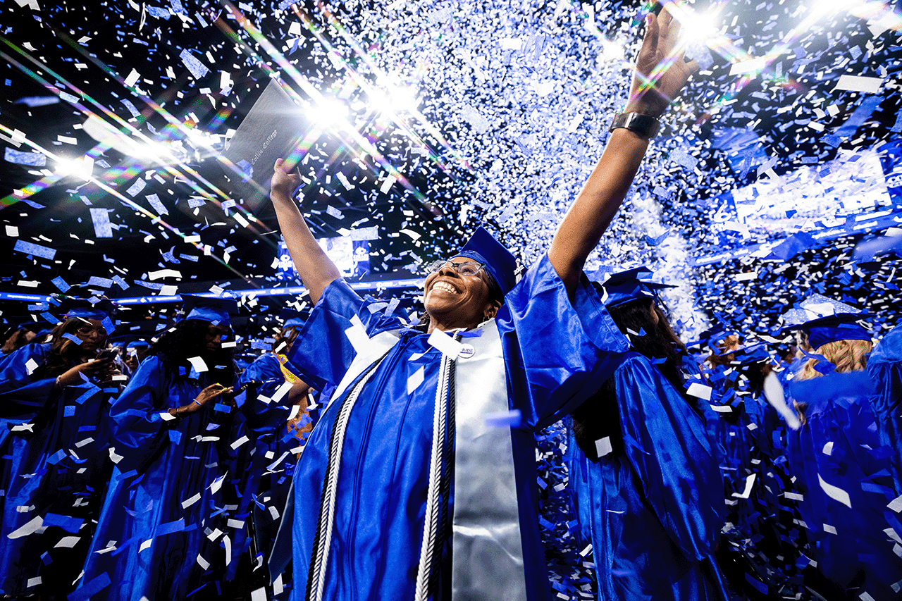 A gradu在e raising their hands up as confetti rains from the venue ceiling