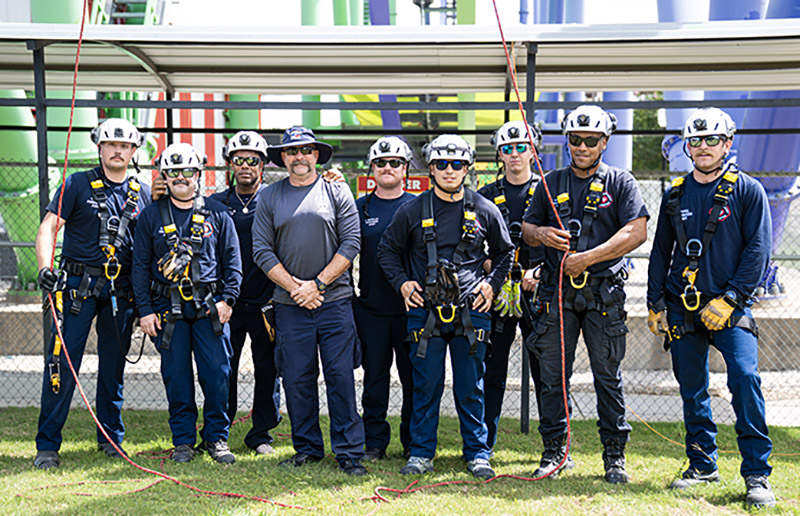 Arlington firefighters stand with Collin College Fire Science Instructor Brian Luyster in front of a Six Flags rollercoaster during a three-day training event.