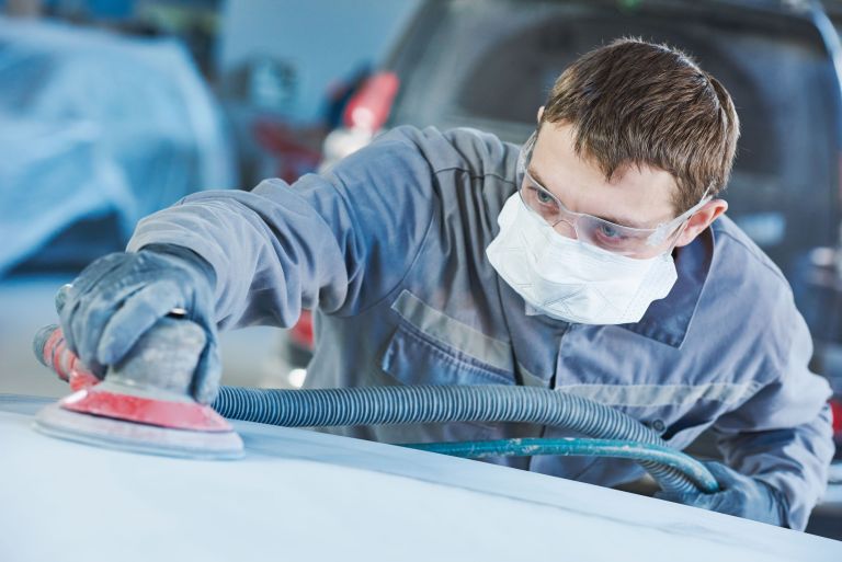 An auto repairman grinding an autobody bonnet