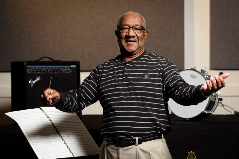 Travis Smith, Adjunct Faculty of Music at Collin College, poses in a conducting stance surrounded by musical equipment.