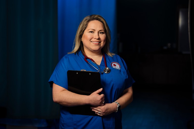 Collin College Medical Assisting Alum Kristen Ostertag poses in her scrubs while holding a clipboard.