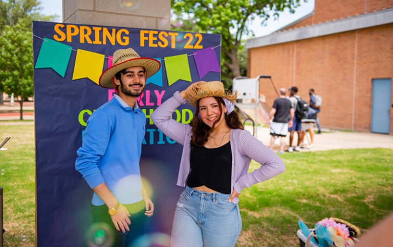 Two Collin College students pose for a picture at the Plano Campus SpringFest 2022 wearing matching straw hats.