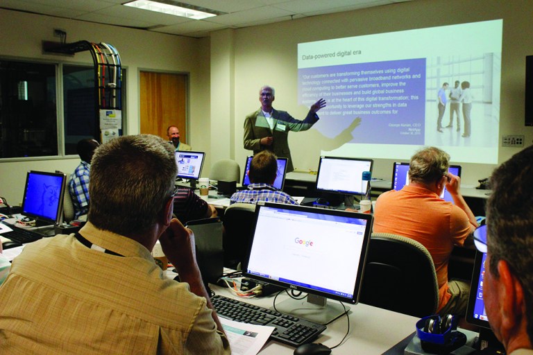 Students sit at computer setups in an IT workshop while being instructed.